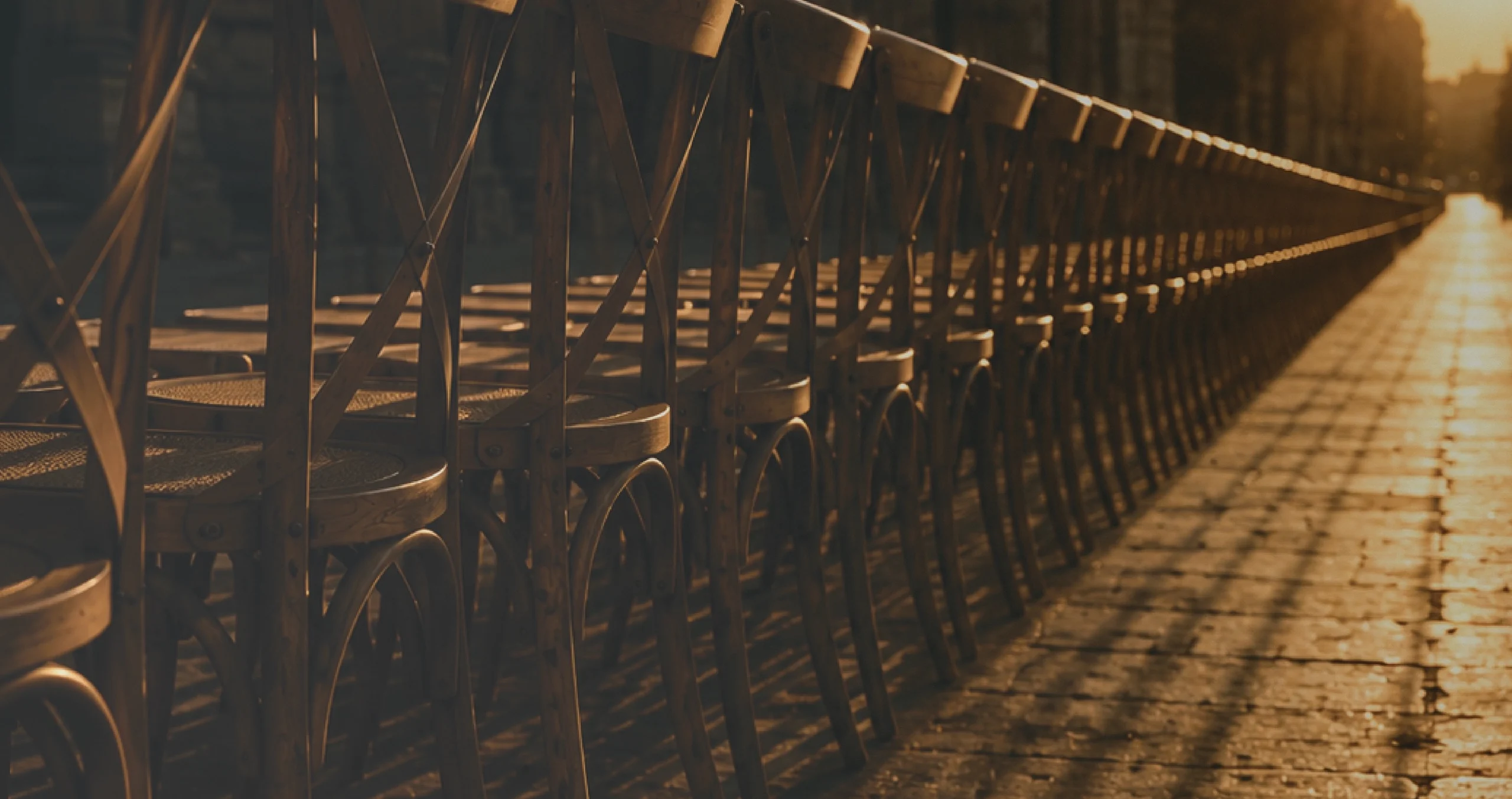 A long row of wooden chairs stretching along the waterfront at golden hour